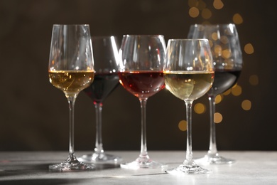 Photo of Glasses with different wines on grey table against defocused lights