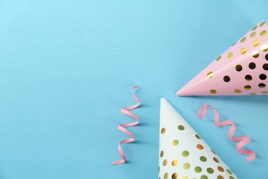 Bright party hats and serpentine streamers on light blue background, flat lay. Space for text