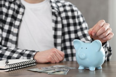 Photo of Financial savings. Man putting coin into piggy bank at wooden table, closeup