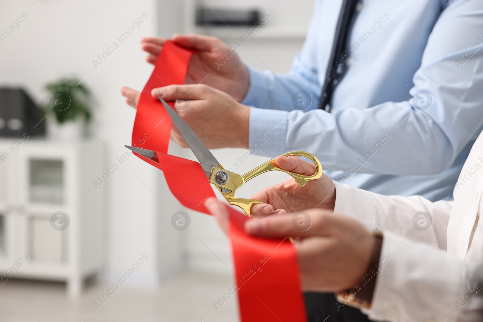 Photo of People cutting red ribbon with scissors indoors, closeup