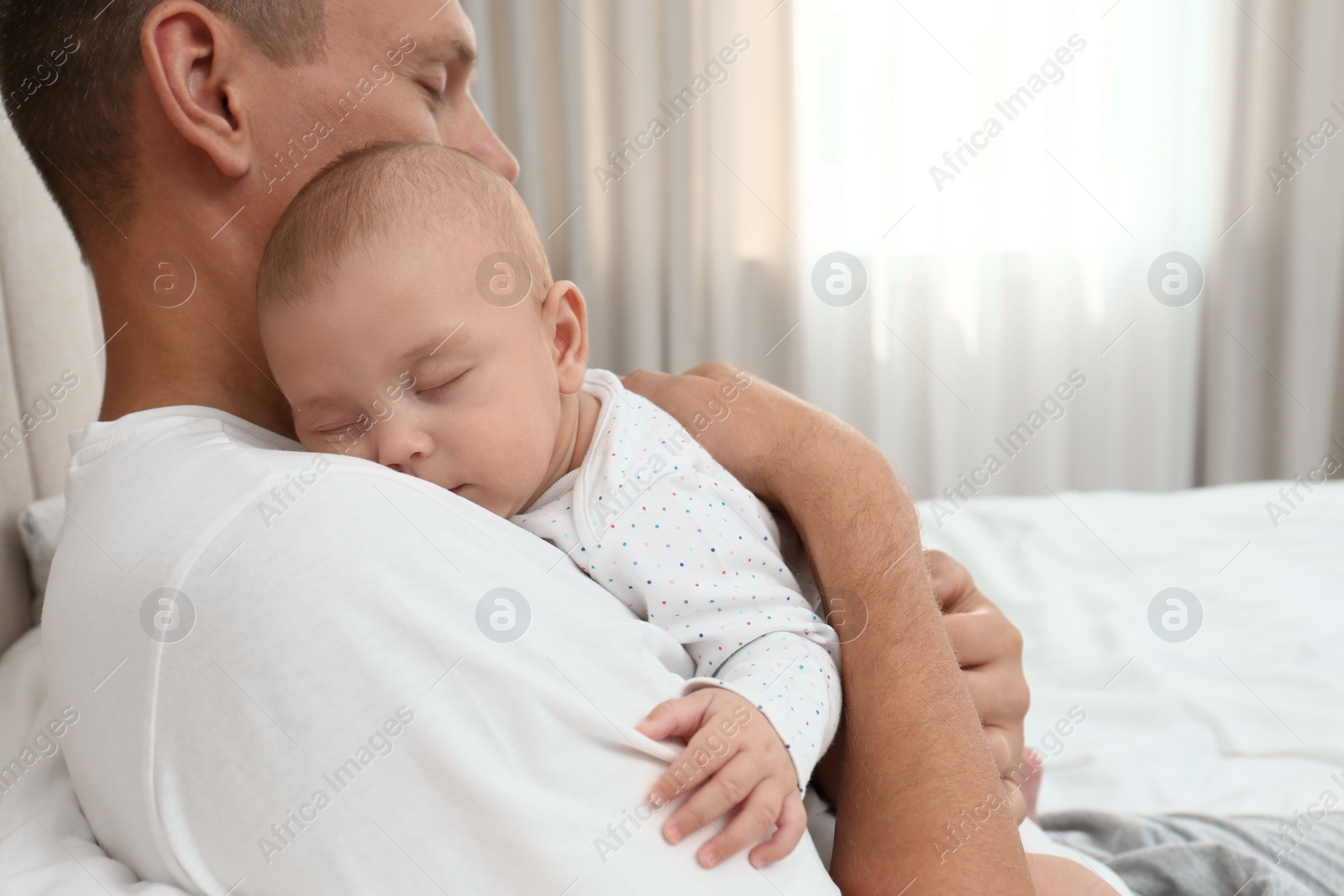 Photo of Father holding his cute sleeping baby on bed at home