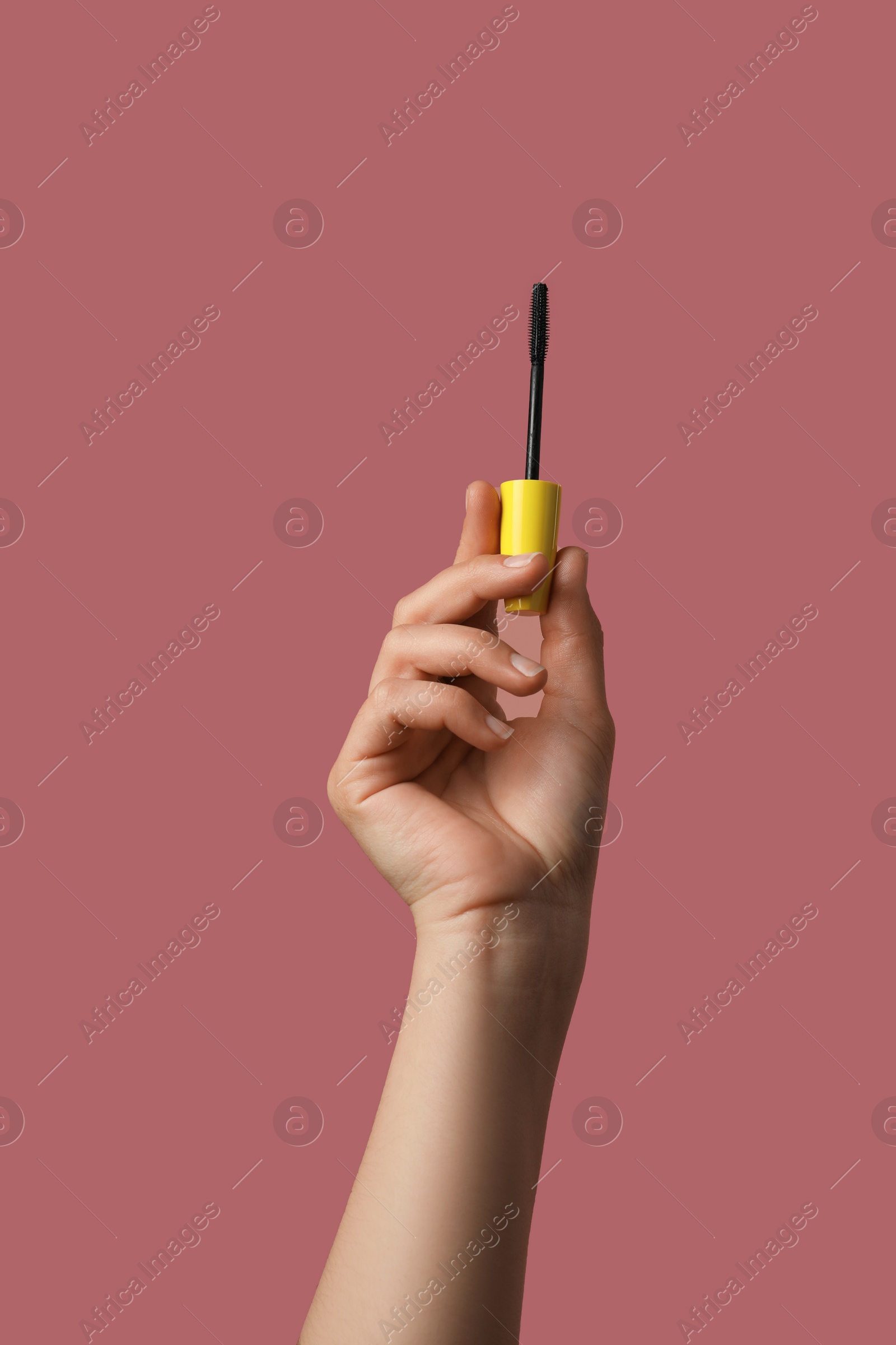 Photo of Woman holding mascara for eyelashes on dusty rose background, closeup