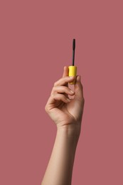 Woman holding mascara for eyelashes on dusty rose background, closeup