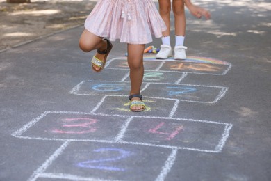 Little children playing hopscotch drawn with chalk on asphalt outdoors, closeup