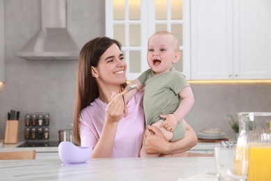 Happy young woman feeding her cute little baby at table in kitchen