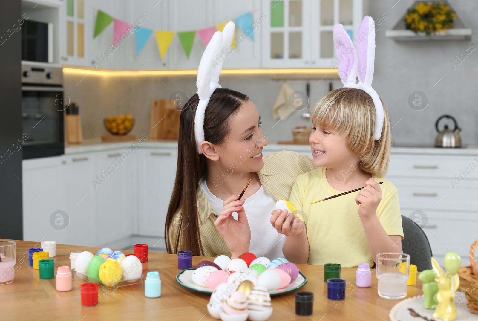 Photo of Mother and her cute son painting Easter eggs at table in kitchen