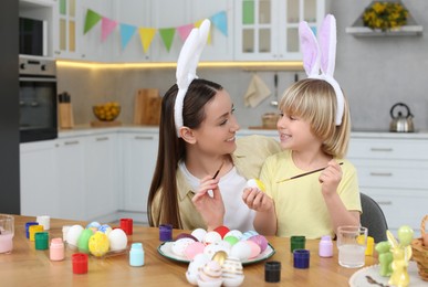 Photo of Mother and her cute son painting Easter eggs at table in kitchen