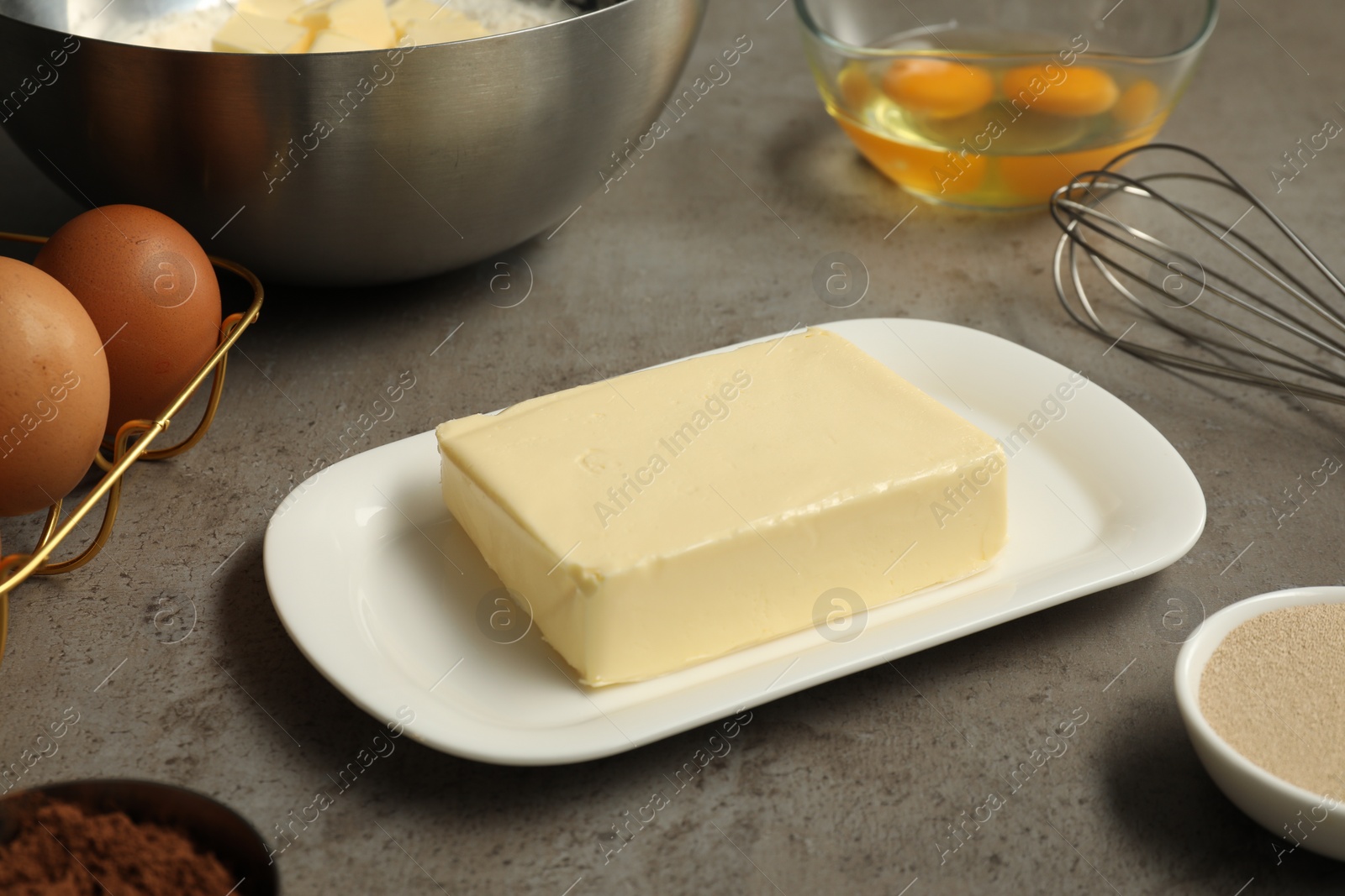 Photo of Fresh butter among other products on grey textured table, closeup