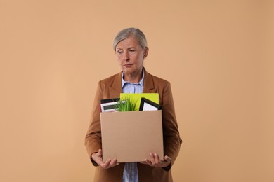 Photo of Unemployed senior woman with box of personal office belongings on beige background