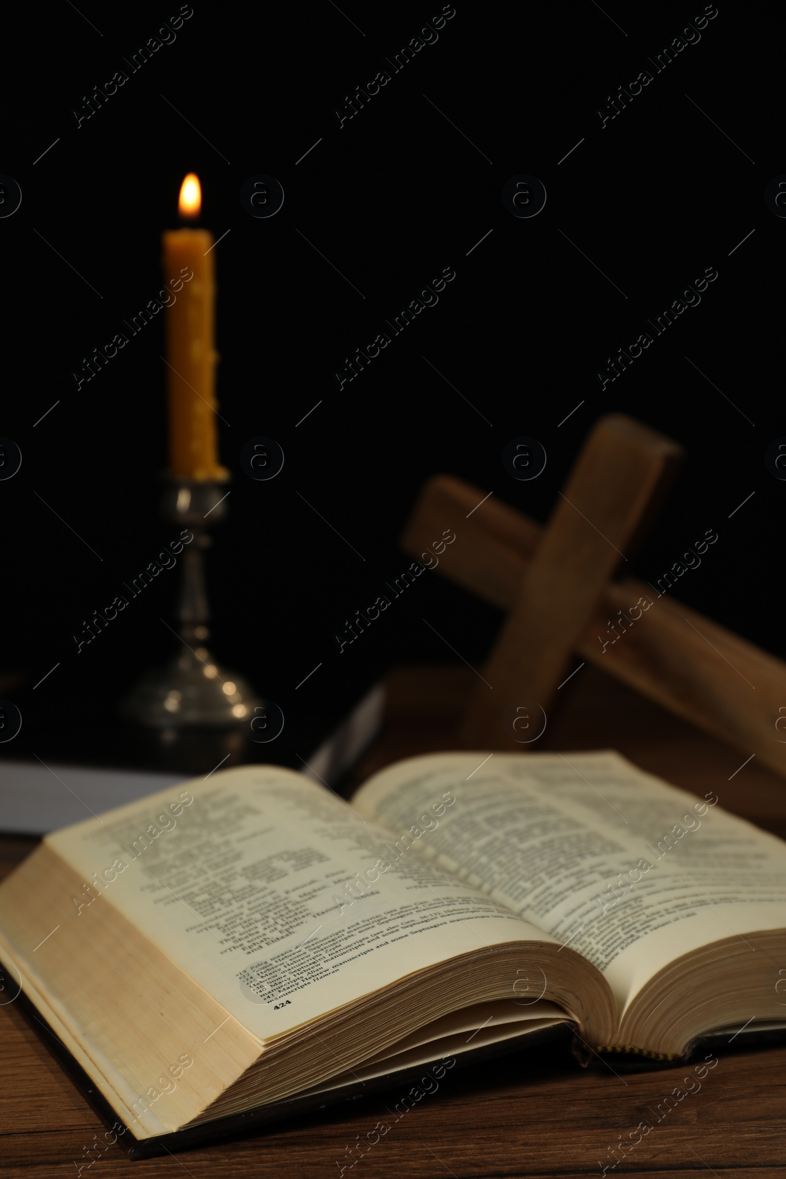 Photo of Church candle, Bible and cross on wooden table against black background