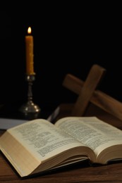 Photo of Church candle, Bible and cross on wooden table against black background