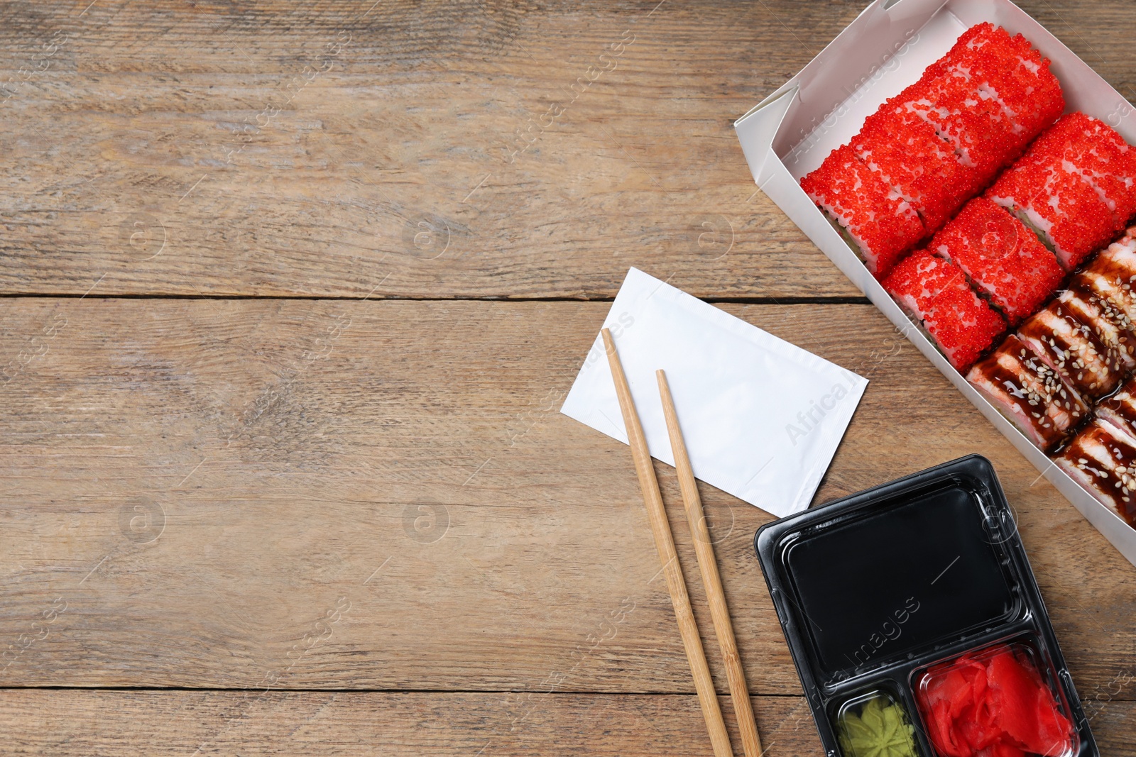 Photo of Food delivery. Delicious sushi rolls served on wooden table, flat lay with space for text