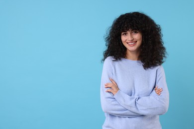 Happy young woman in stylish warm sweater on light blue background, space for text