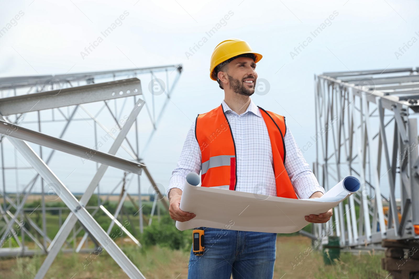 Photo of Professional engineer with plan near high voltage tower construction outdoors. Installation of electrical substation