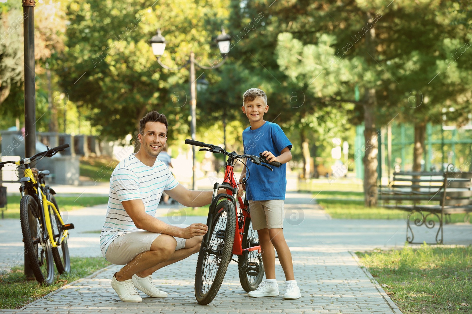 Photo of Dad and son fixing bicycle in park on sunny day