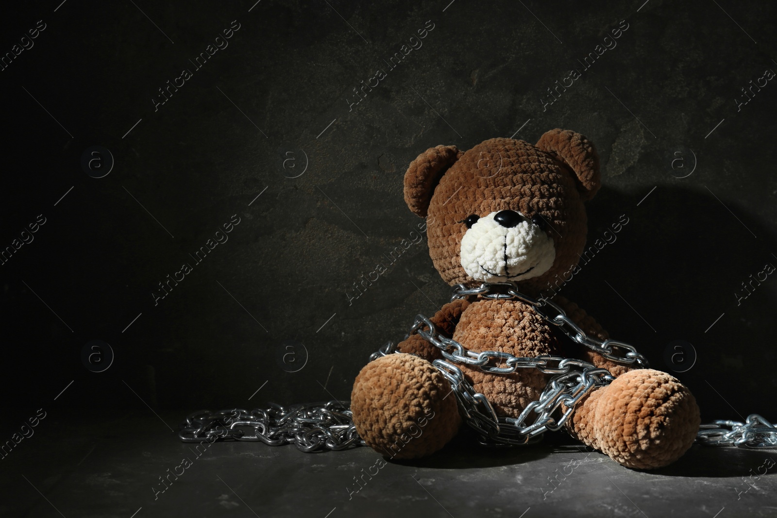 Photo of Stop child abuse. Chained toy bear in dark room. Space for text