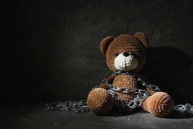Photo of Stop child abuse. Chained toy bear in dark room. Space for text