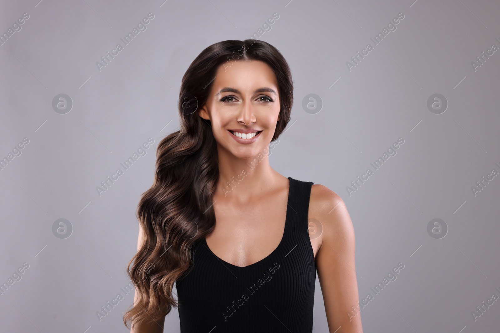 Image of Gorgeous woman with shiny wavy hair on grey background. Professional hairstyling