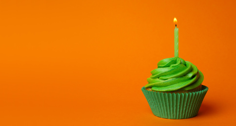 Delicious birthday cupcake with green cream and burning candle on orange background. Space for text