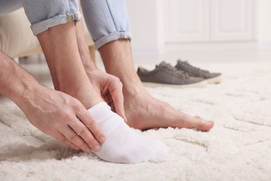 Photo of Man putting on white sock at home, closeup. Space for text