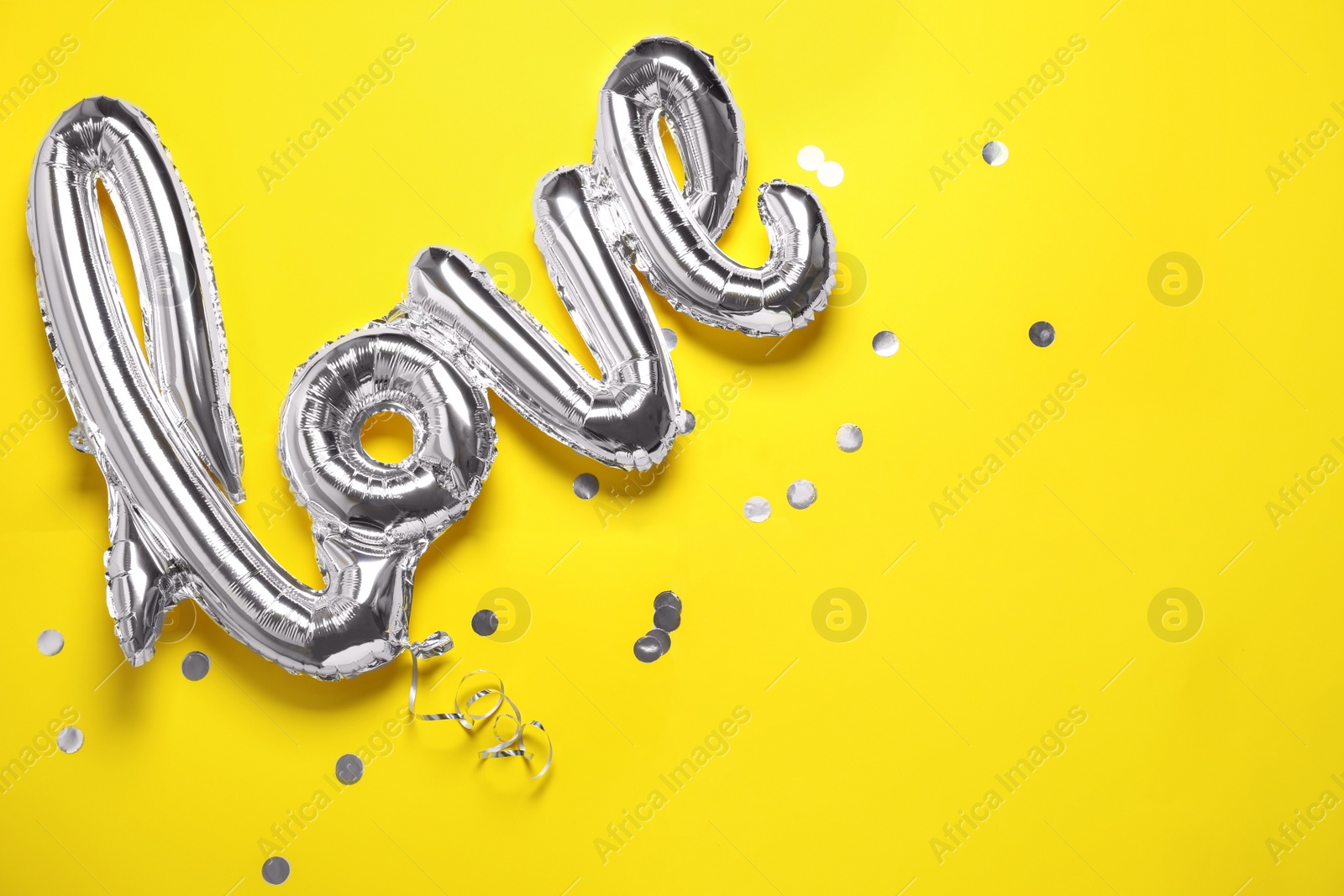 Photo of Foil LOVE word balloon and confetti on yellow background, flat lay