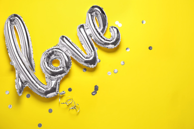 Foil LOVE word balloon and confetti on yellow background, flat lay