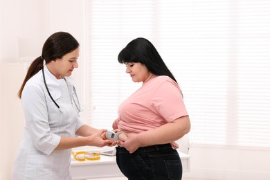 Photo of Nutritionist measuring overweight woman's body fat layer with caliper in clinic