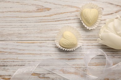 Delicious heart shaped chocolate candies and beautiful tulip on white wooden table, flat lay. Space for text