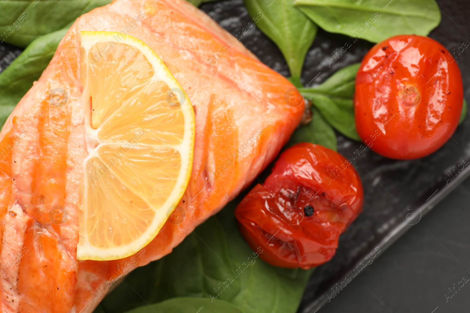 Photo of Tasty grilled salmon with tomatoes and spinach on table, top view