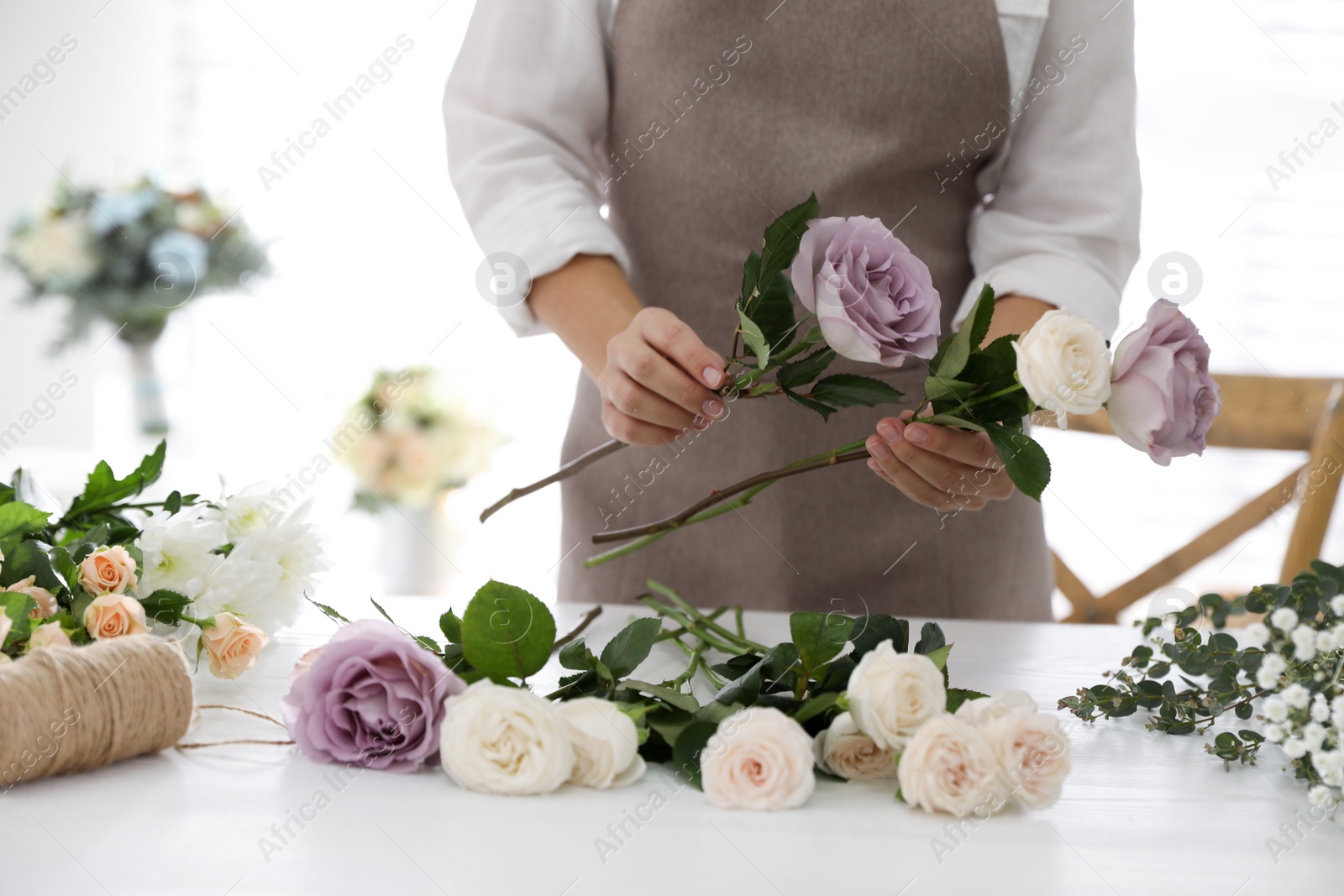 Photo of Florist making beautiful wedding bouquet at white table, closeup