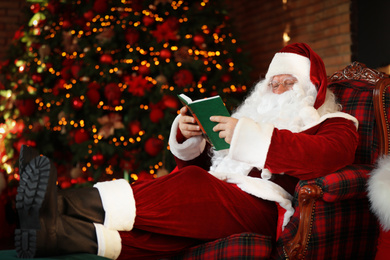 Santa Claus reading book near decorated Christmas tree indoors