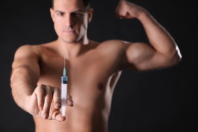 Photo of Athletic man with syringe against black background, focus on hand. Doping concept