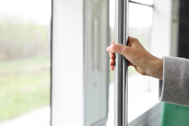 Photo of Woman holding grab pole near window in public transport, closeup. Space for text