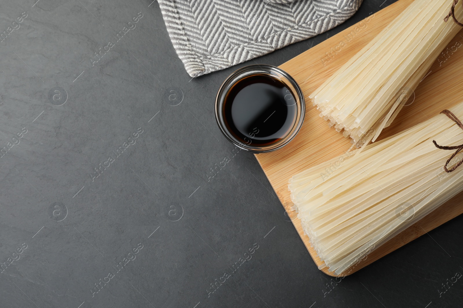 Photo of Dried rice noodles with soy sauce on black table, top view. Space for text