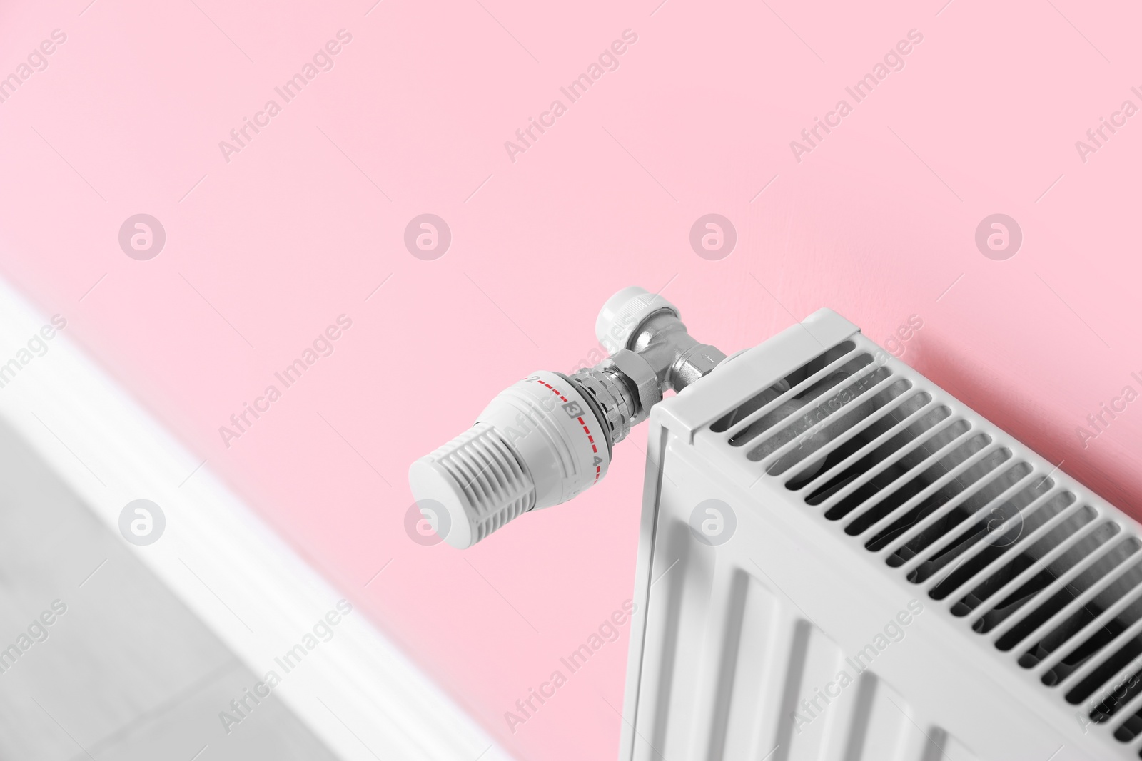 Photo of Heating radiator with thermostat near color wall