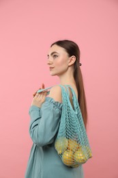 Photo of Woman with string bag of fresh lemons on pink background