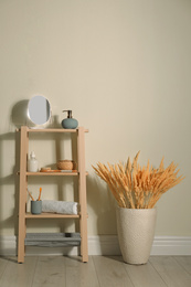 Wooden shelving unit with toiletries near light wall indoors. Bathroom interior element