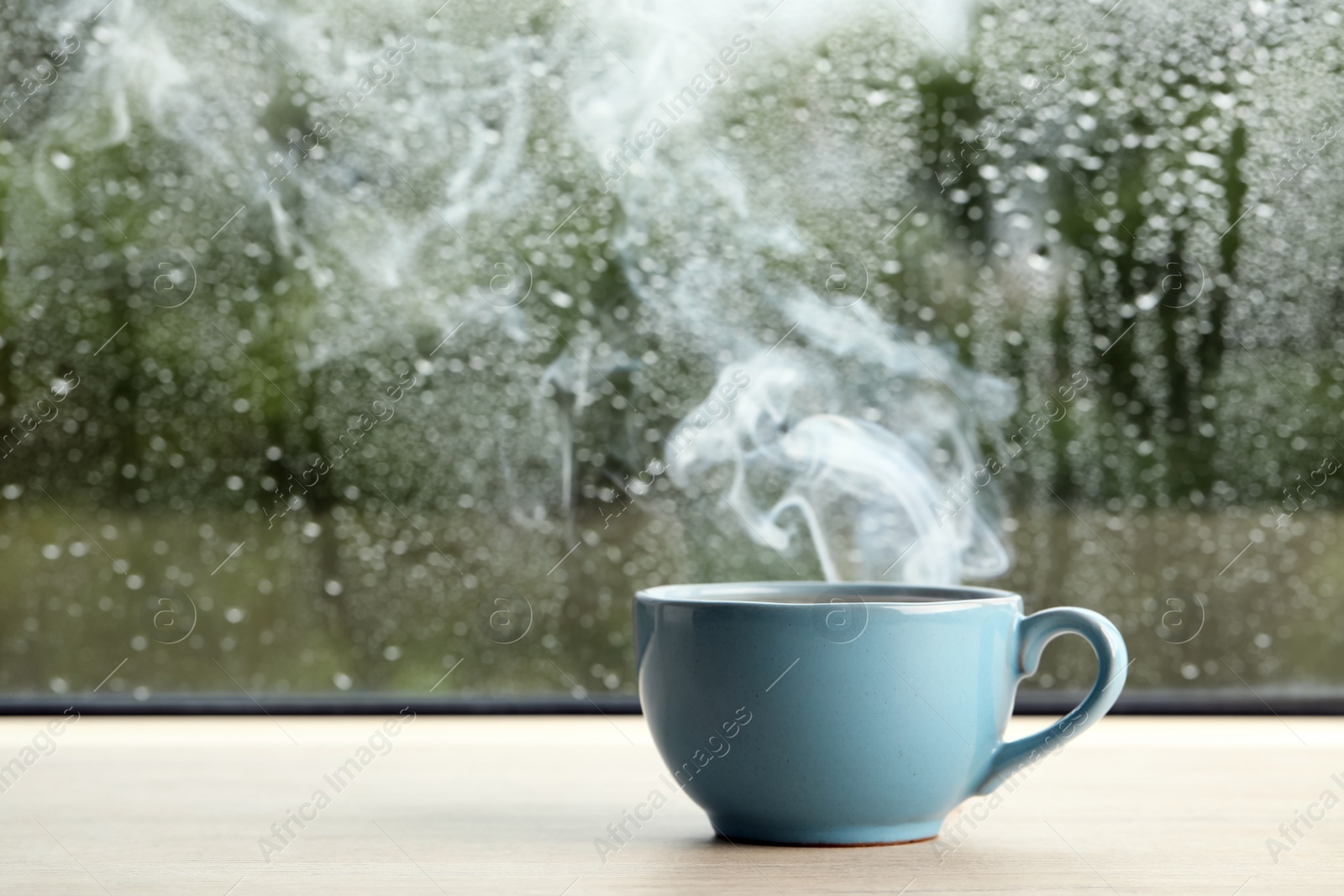 Photo of Cup of hot drink near window on rainy day. Space for text