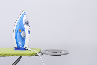 Photo of Modern electric iron on board against light background, space for text