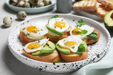 Photo of Tasty bruschettas with quail eggs and avocado on light grey marble table