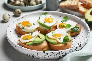 Tasty bruschettas with quail eggs and avocado on light grey marble table