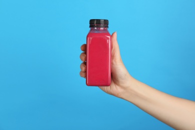 Woman holding bottle with delicious smoothie on color background