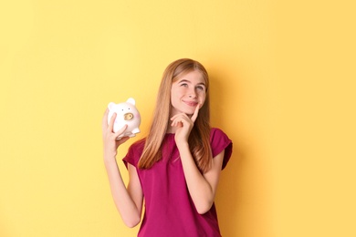 Teen girl with piggy bank on color background