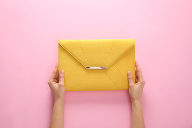 Woman holding stylish envelope bag on pink background, closeup