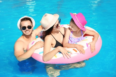 Young family with little daughter in swimming pool on sunny day