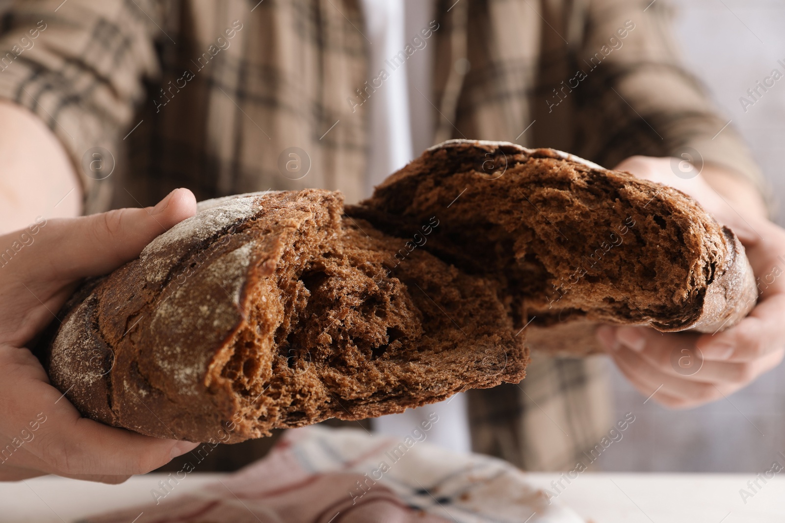 Photo of Man breaking loaf of fresh bread on white table, closeup