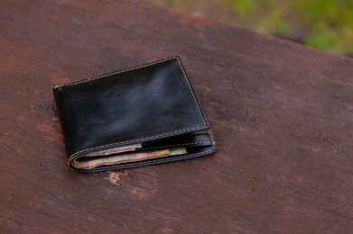 Photo of Black wallet on wooden bench outdoors. Lost and found