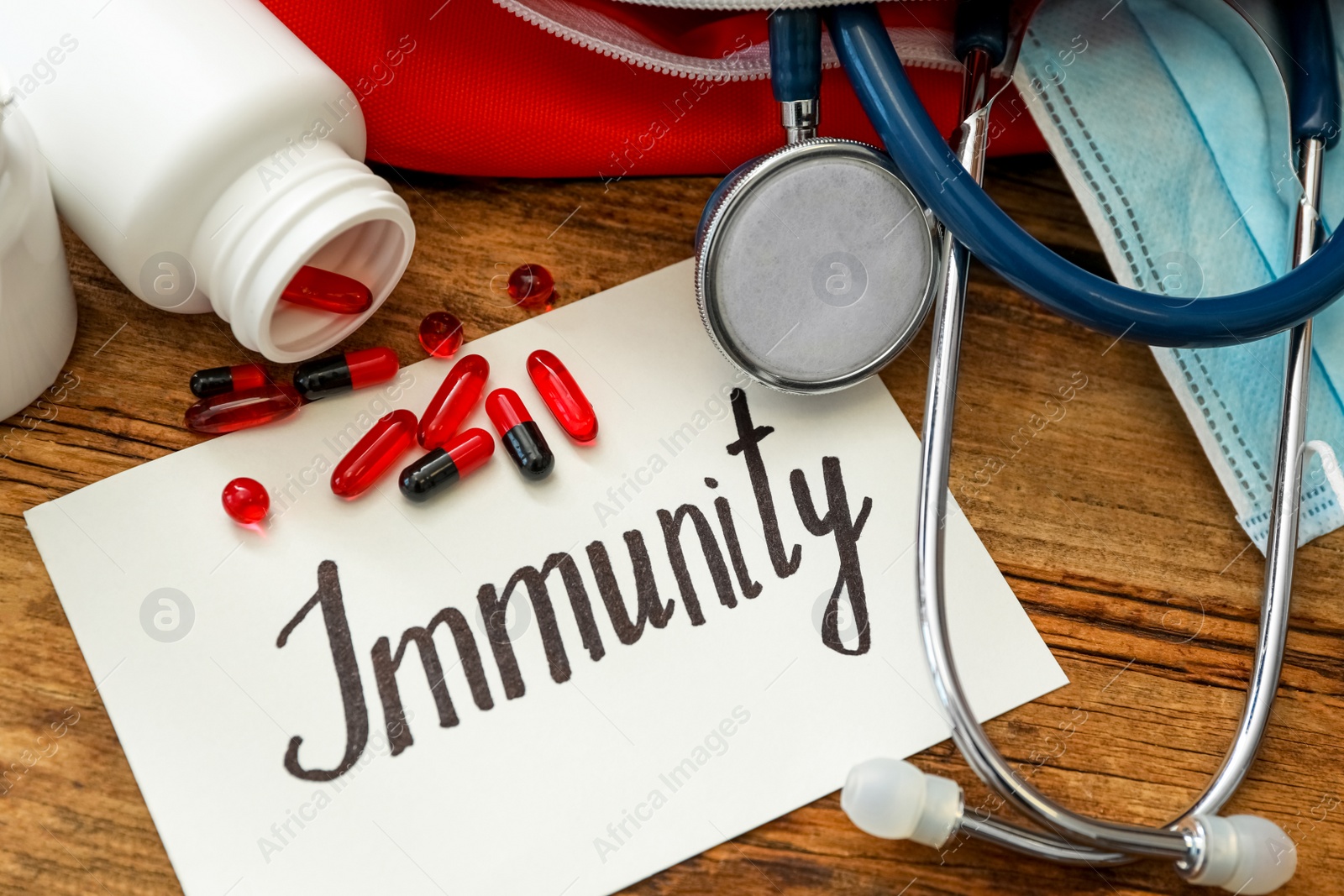 Photo of Paper sheet with word Immunity and first aid kit on wooden table, closeup