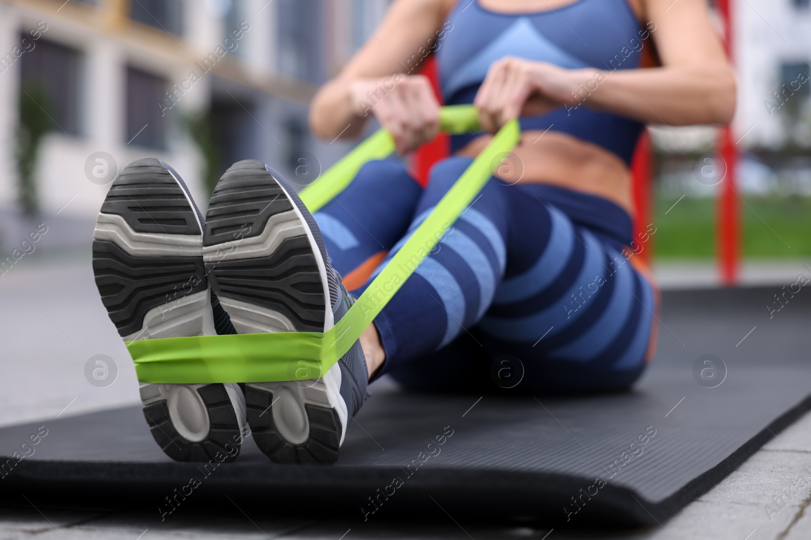 Photo of Woman doing exercise with fitness elastic band on mat outdoors, closeup