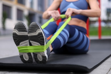 Woman doing exercise with fitness elastic band on mat outdoors, closeup